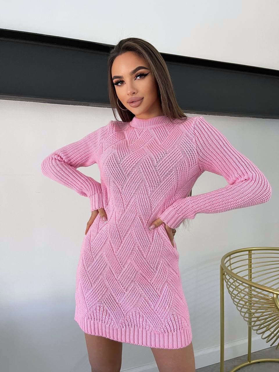 Woman wearing a pink knitted dress against a white wall.