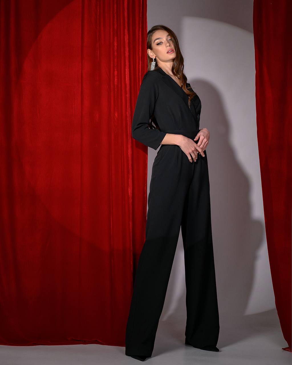 Woman in a black outfit standing against a red curtain backdrop
