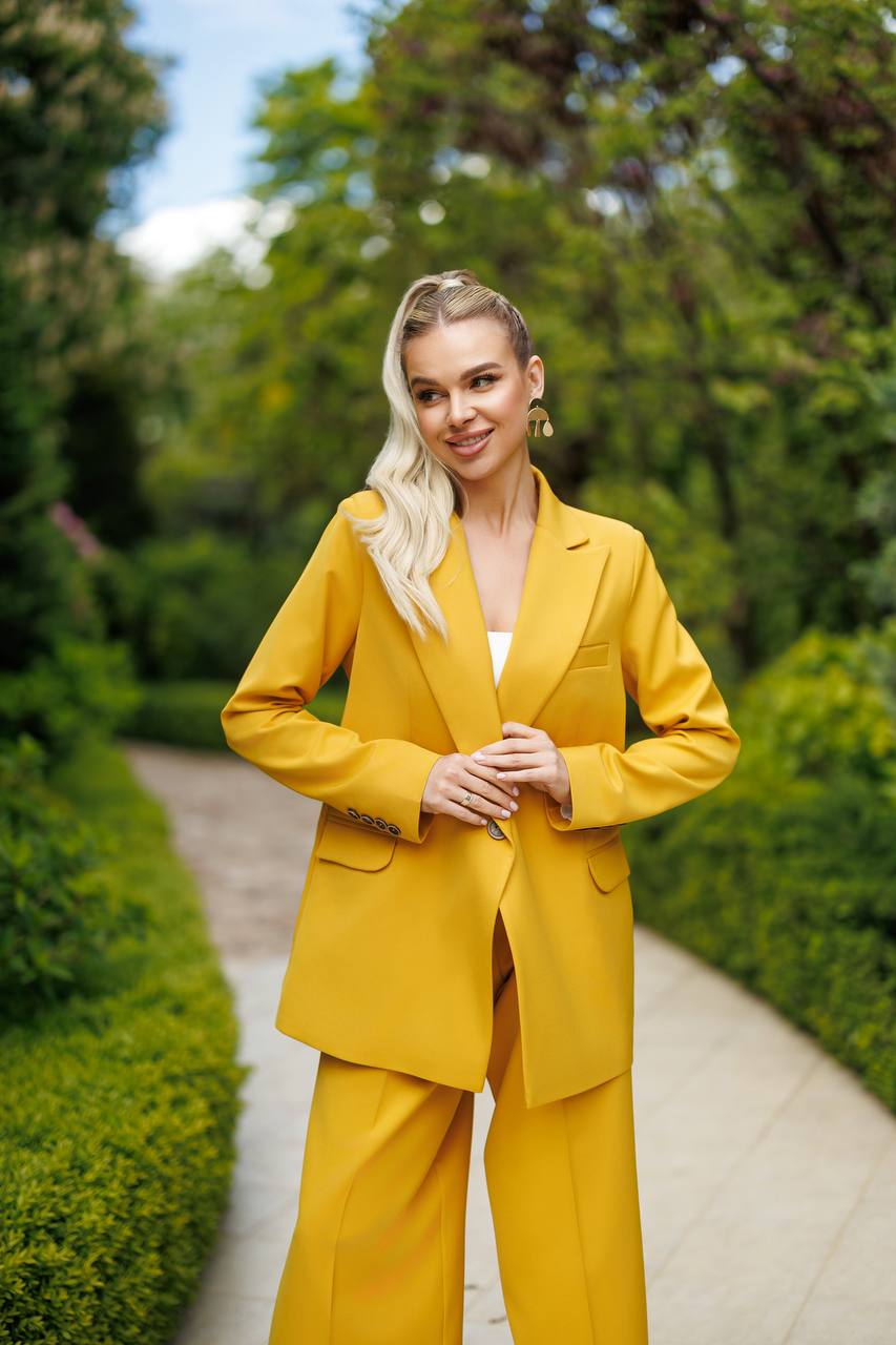Woman in a yellow suit standing on a path with greenery in the background