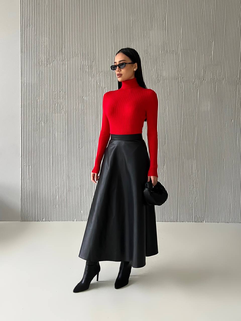 Woman wearing a red turtleneck and black leather skirt against a gray striped background
