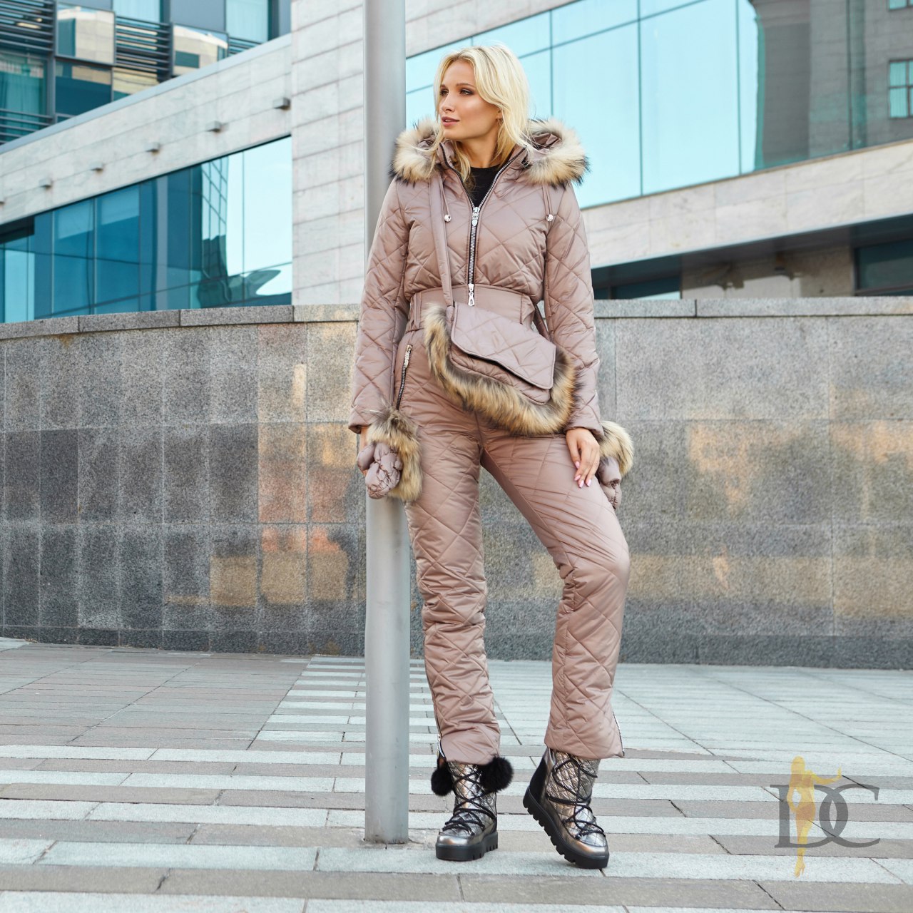 Woman in a pink winter outfit with fur trim standing in an urban setting.