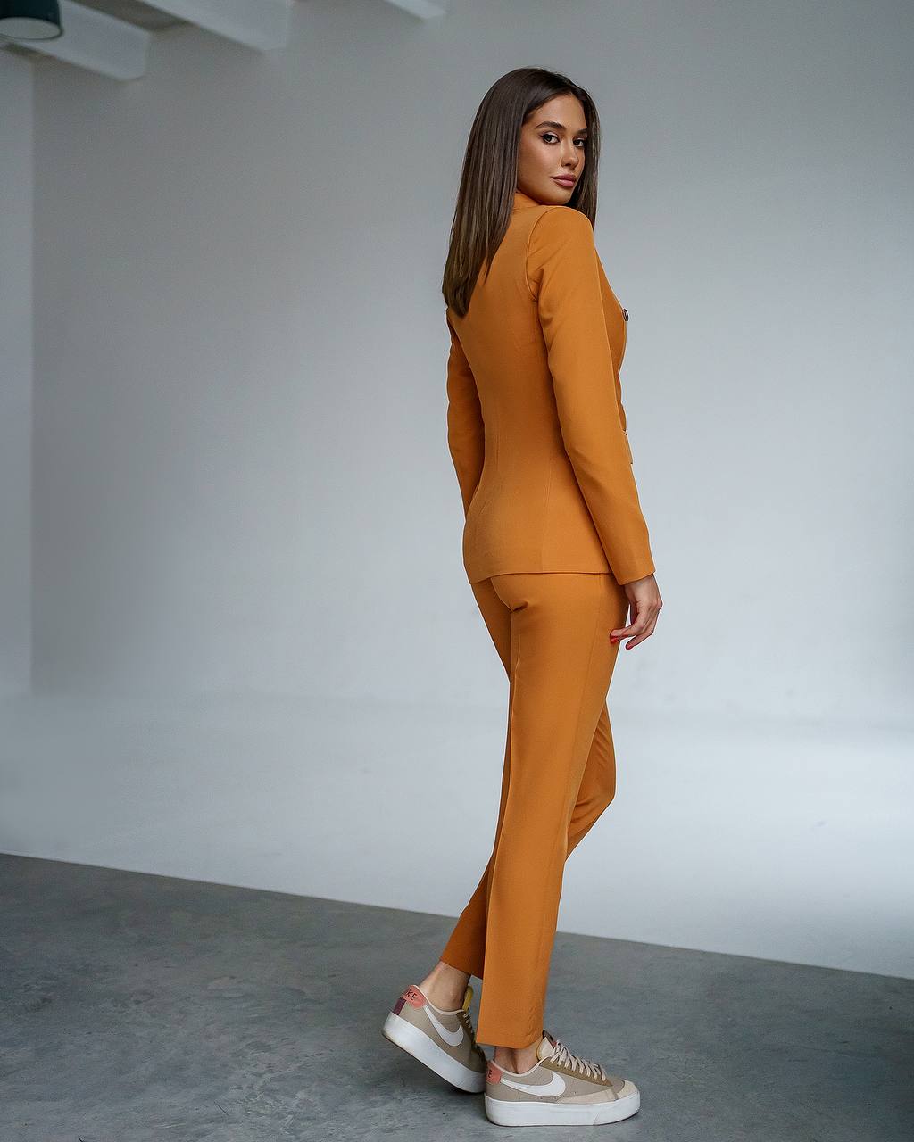 Woman wearing a mustard yellow suit standing against a plain background
