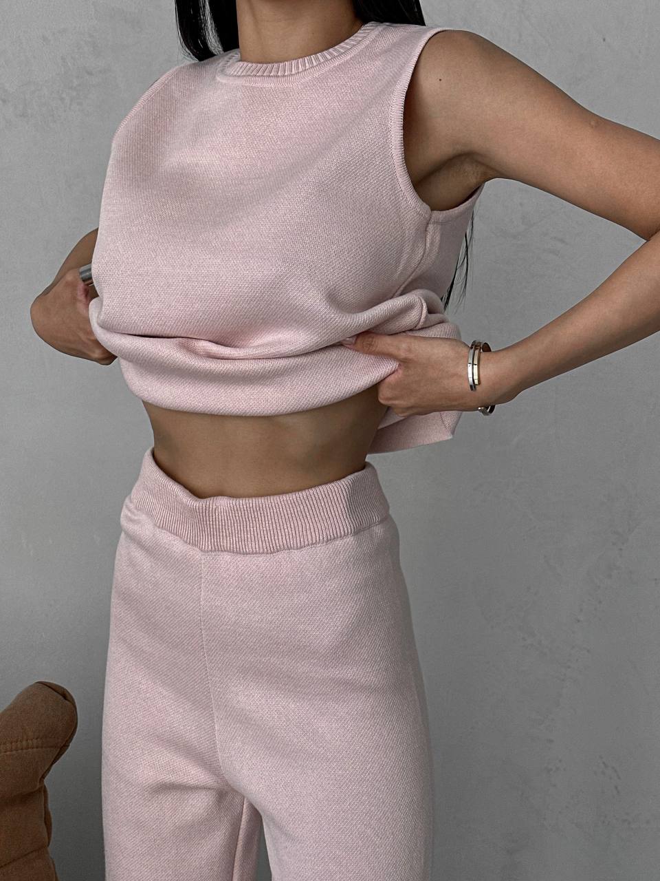 Person wearing a pink sleeveless top and pants against a gray background