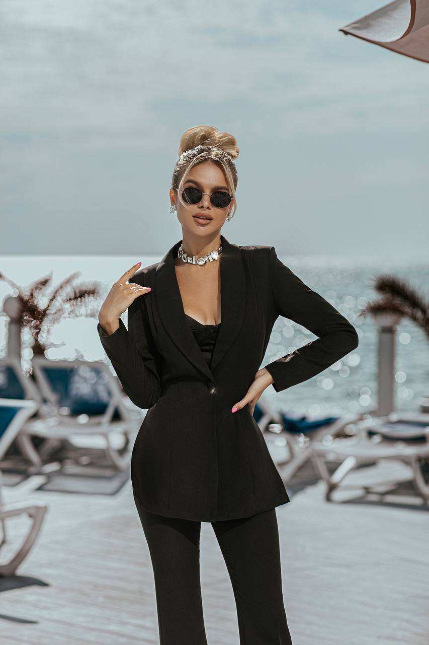Woman in a black suit standing on a beach with ocean view