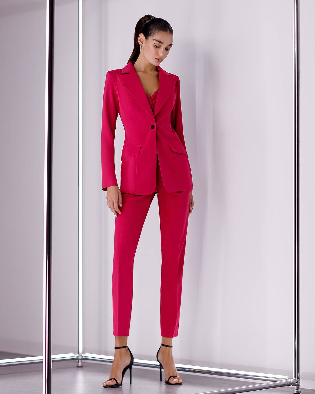 Woman wearing a bright pink suit standing in front of a white curtain.