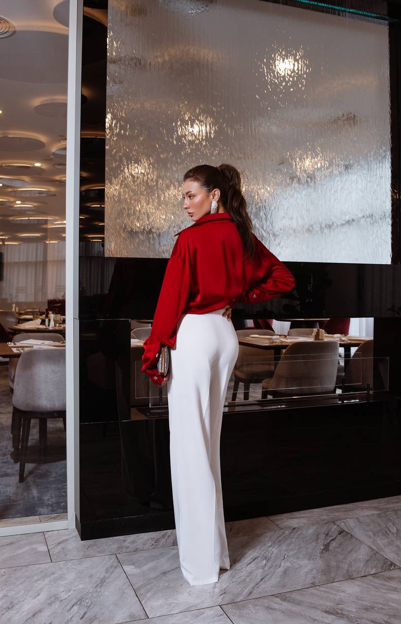 Woman in a red jacket and white pants standing in a modern interior setting.