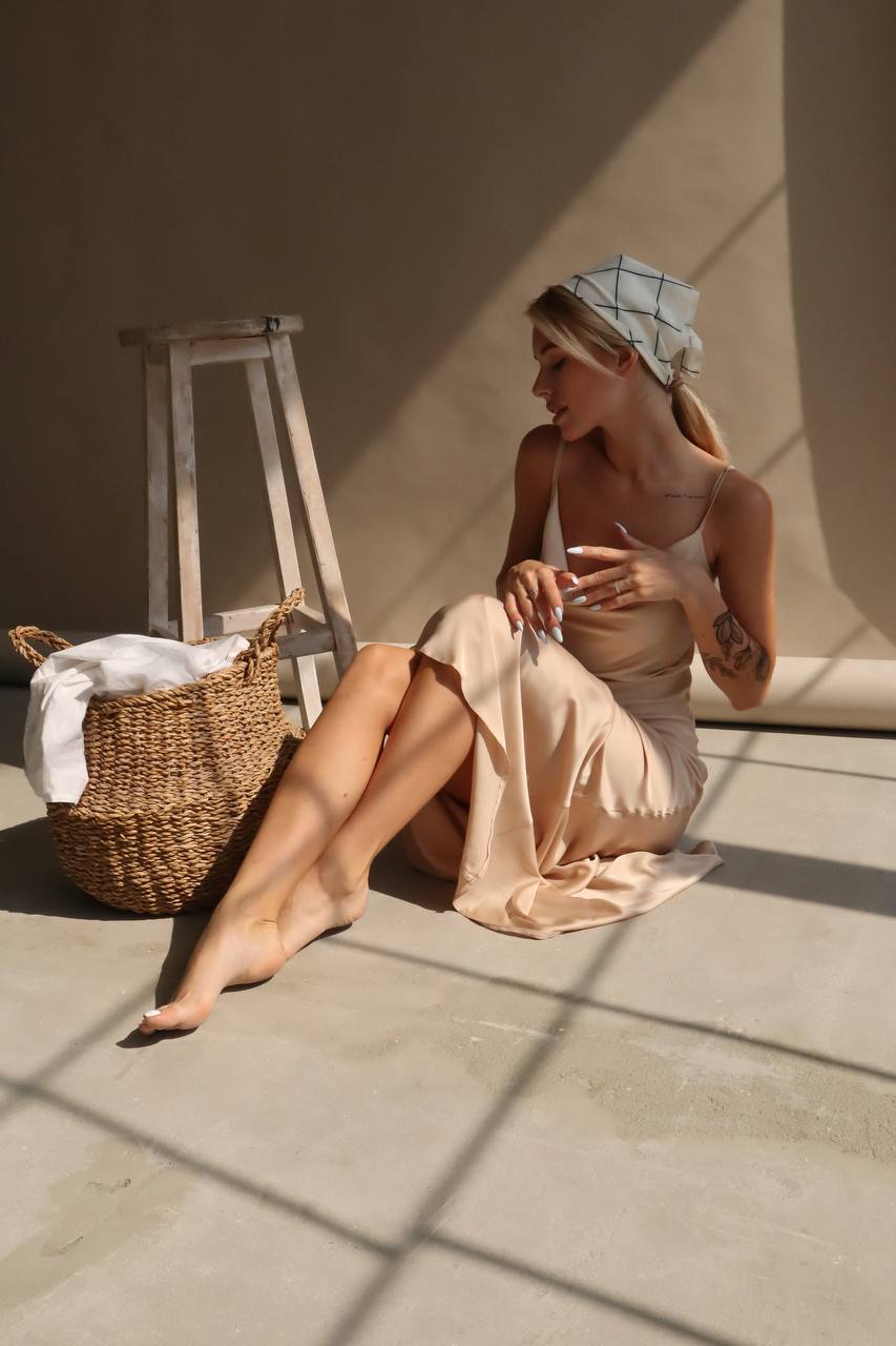 Woman in a beige dress sitting on a stone floor with a woven basket nearby.
