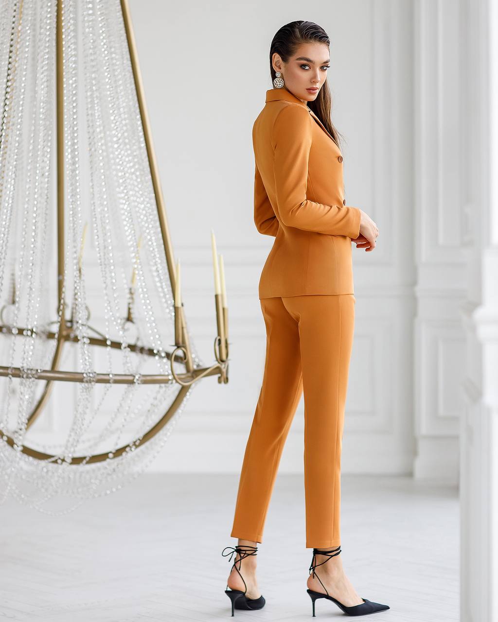 Woman in a mustard yellow outfit standing in a stylish interior setting.