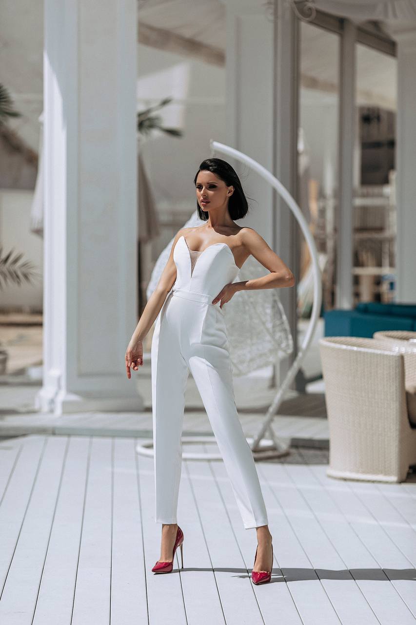 Woman in a white jumpsuit standing on a wooden deck with white columns in the background
