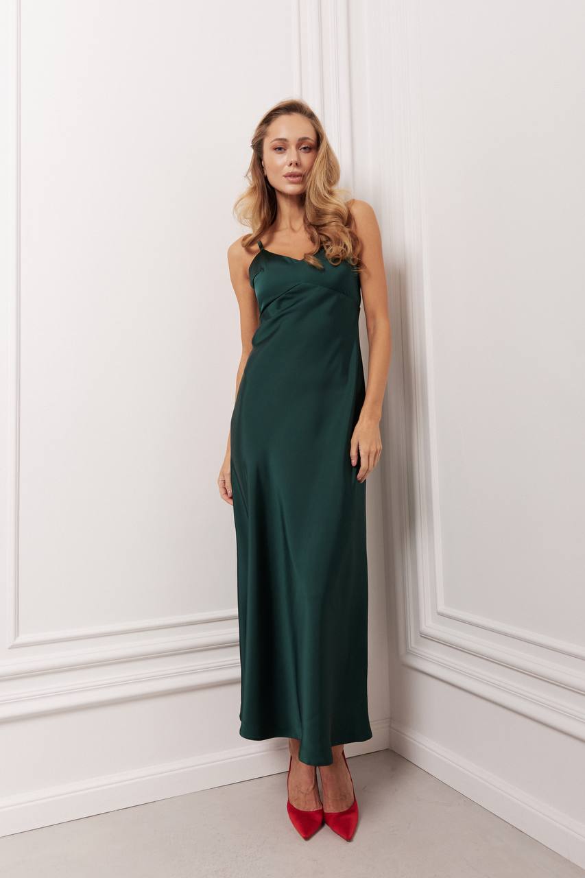 Woman wearing a dark green dress with red shoes against a white wall.