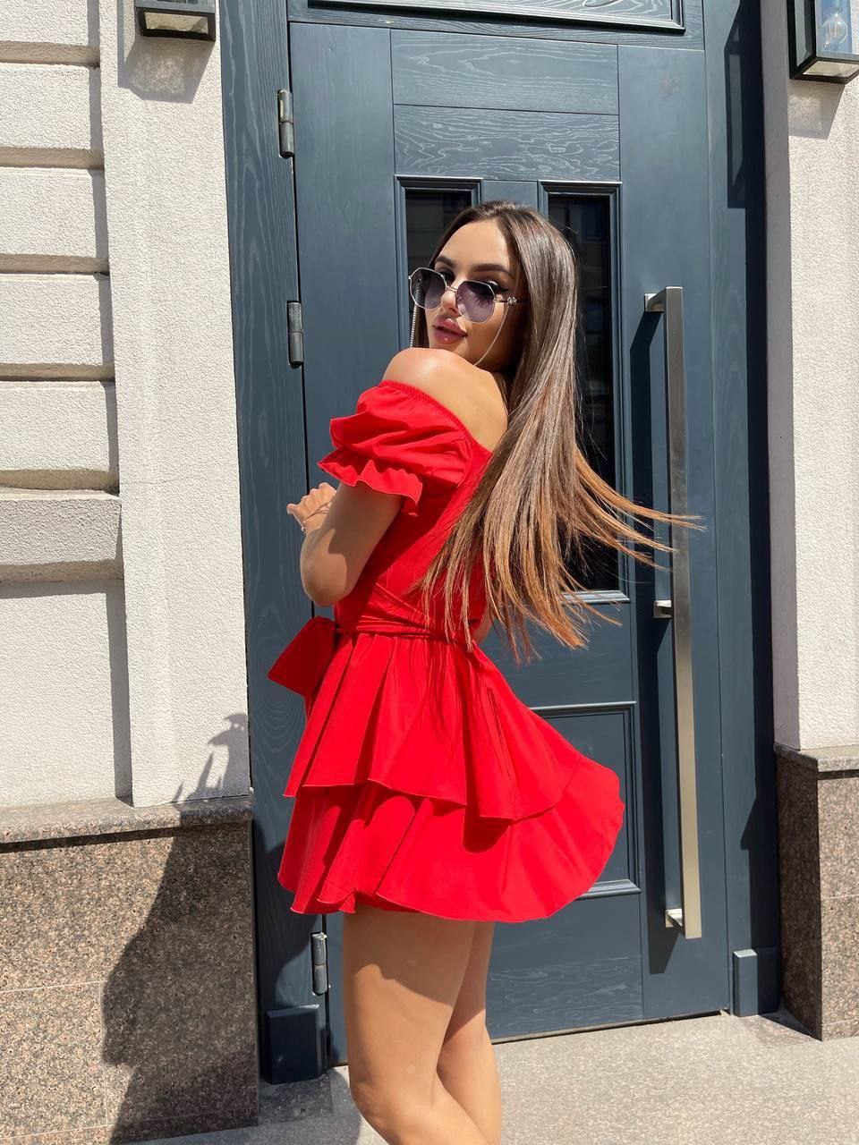 Woman in a red dress standing in front of a gray door.