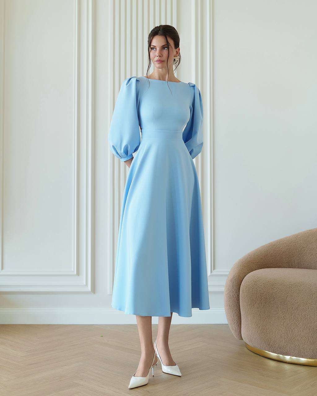 Woman wearing a light blue dress with puffed sleeves in an elegant room.