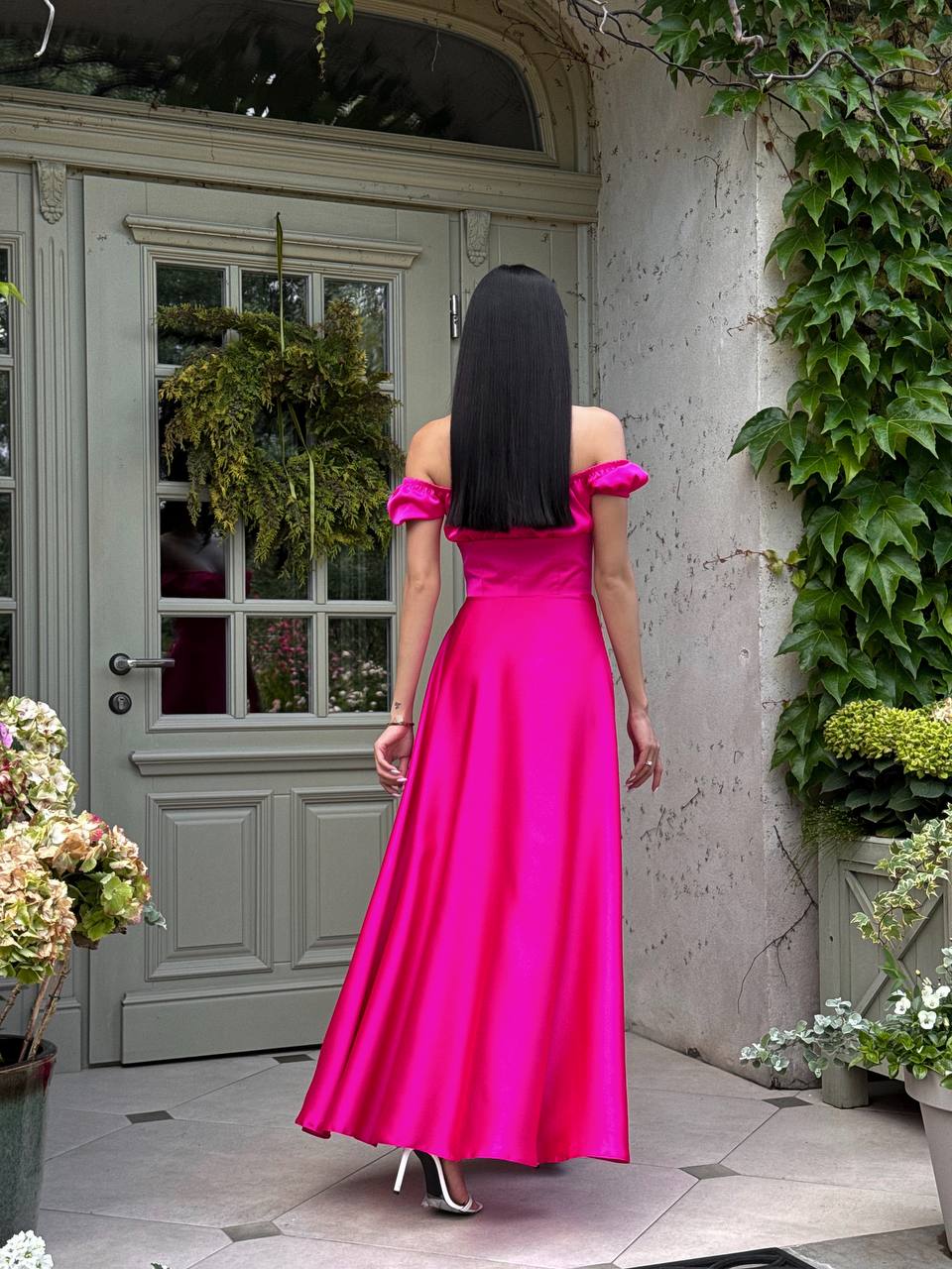 Woman in a bright pink dress standing in front of a gray door with greenery.