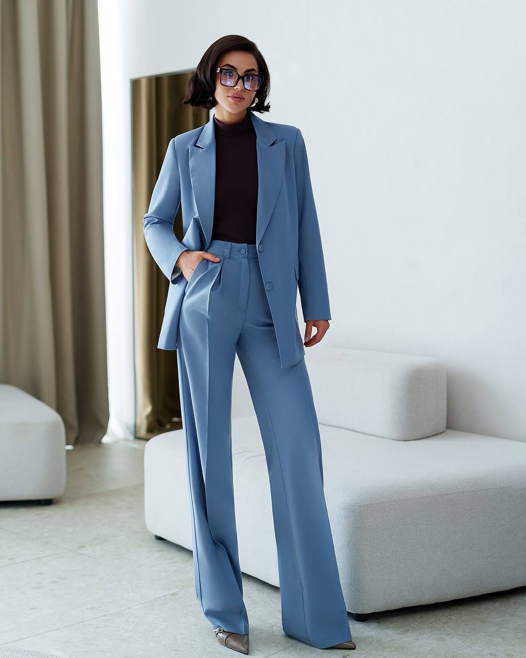 Woman in a blue suit standing in a modern living room.