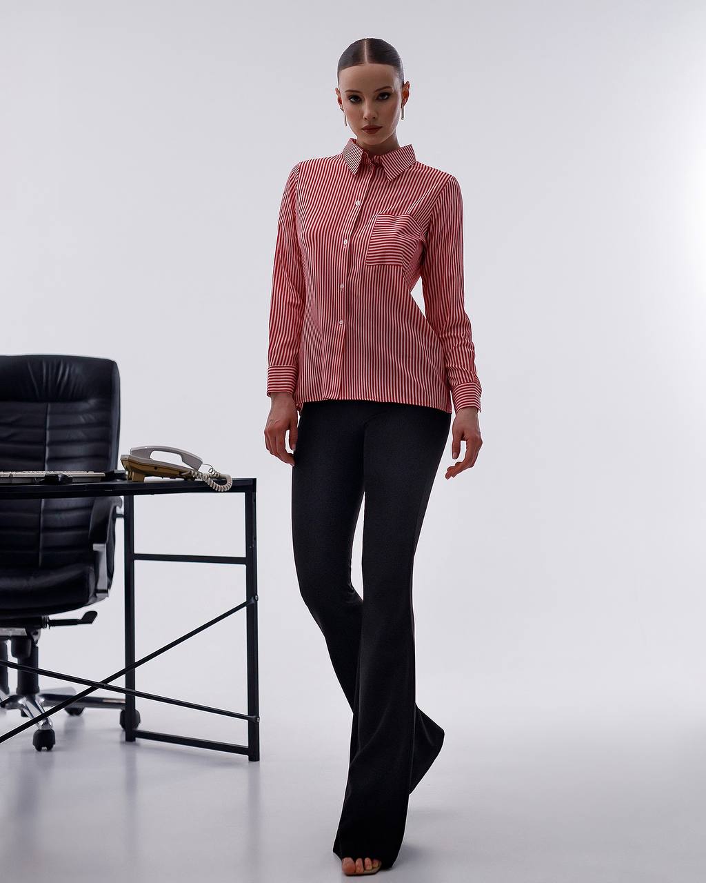 Woman wearing a red striped shirt and black pants standing in an office setting.