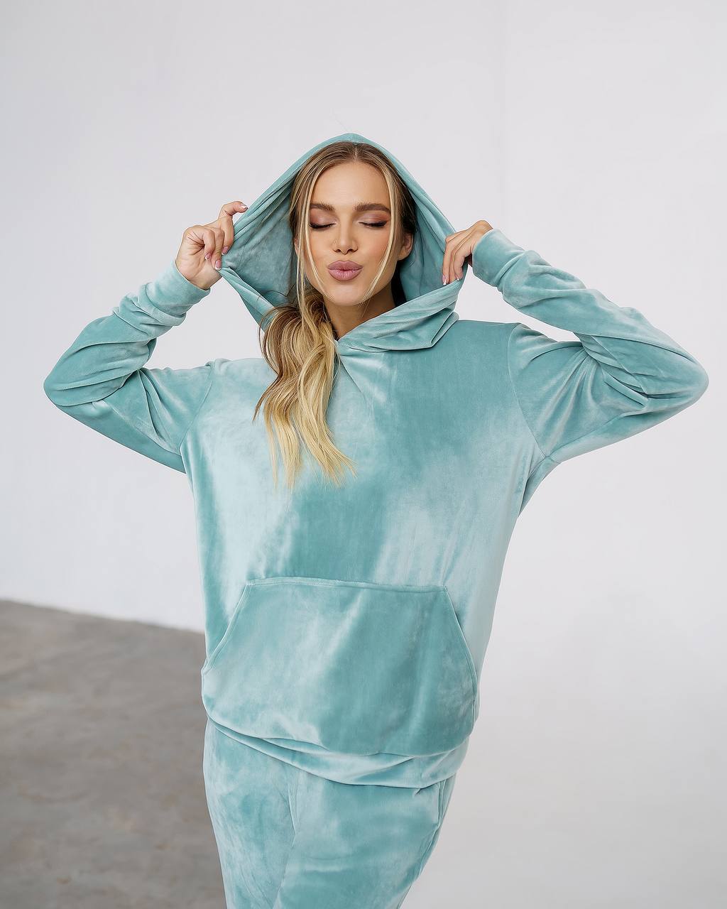 Person wearing a teal velour hoodie and pants against a white background