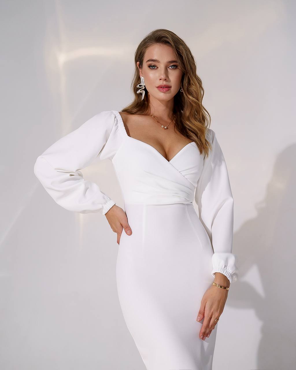 Woman wearing a white dress with long sleeves against a plain background