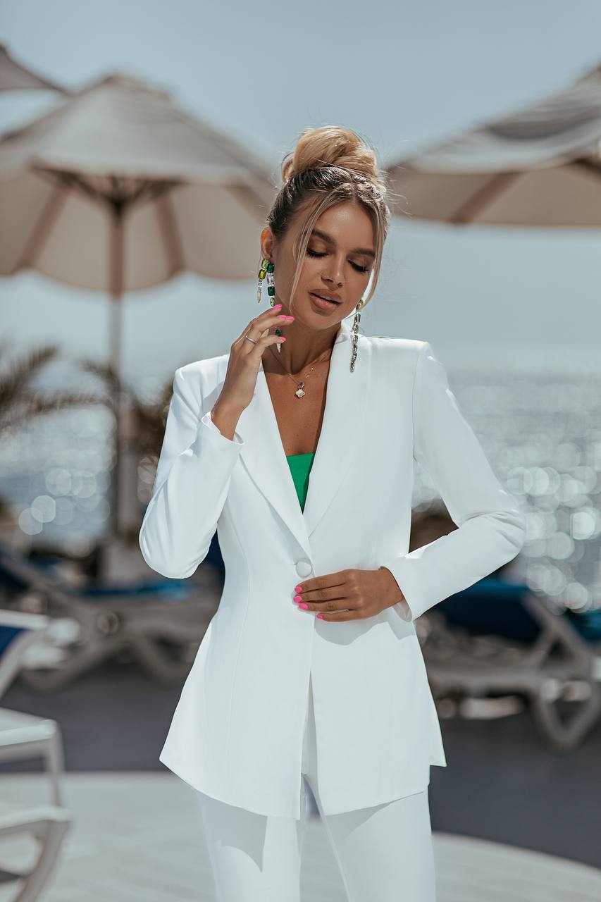 Woman in a white suit standing on a beach with umbrellas and chairs in the background