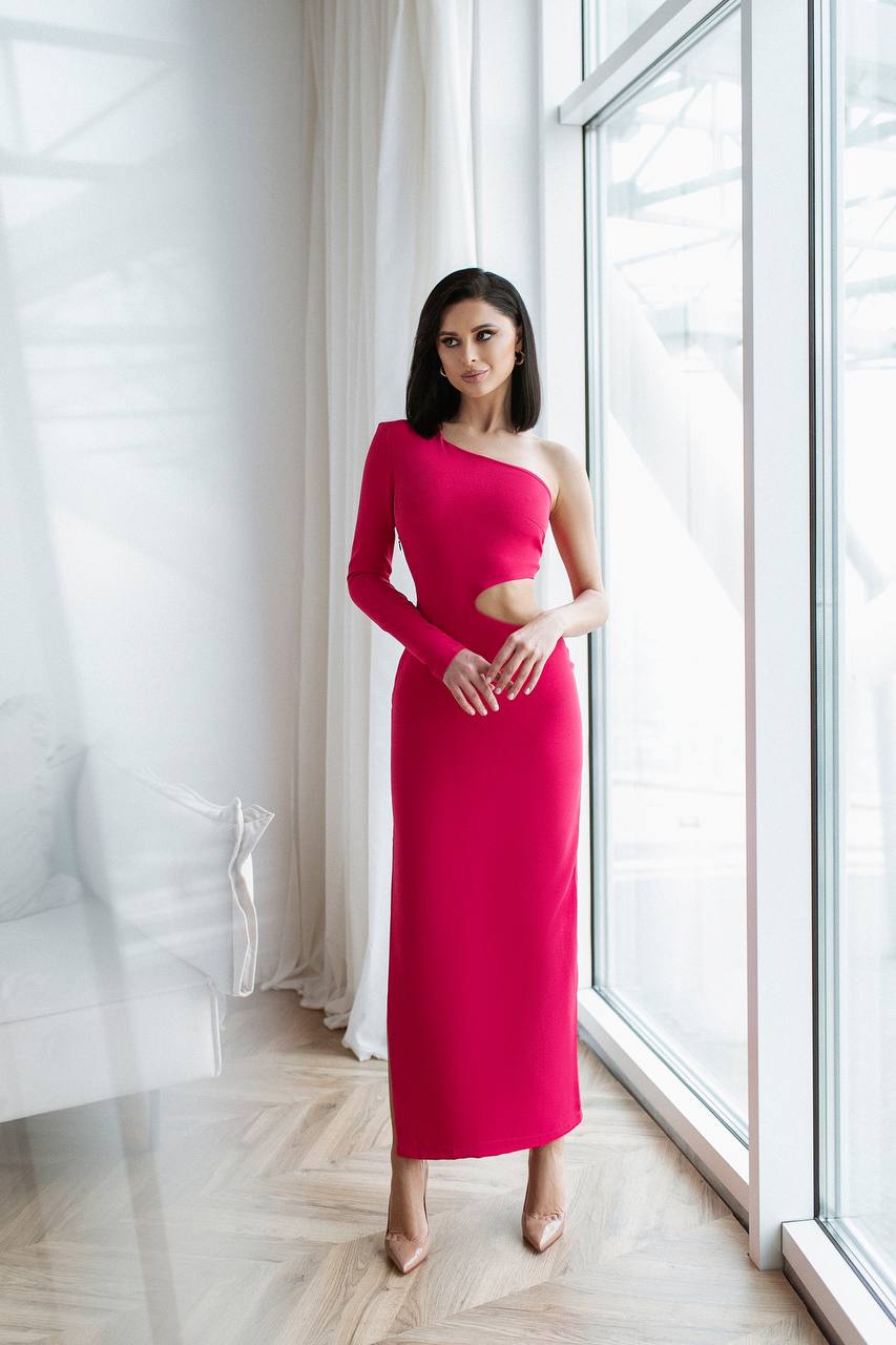 Woman in a pink one-shoulder dress standing in a bright room with large windows.