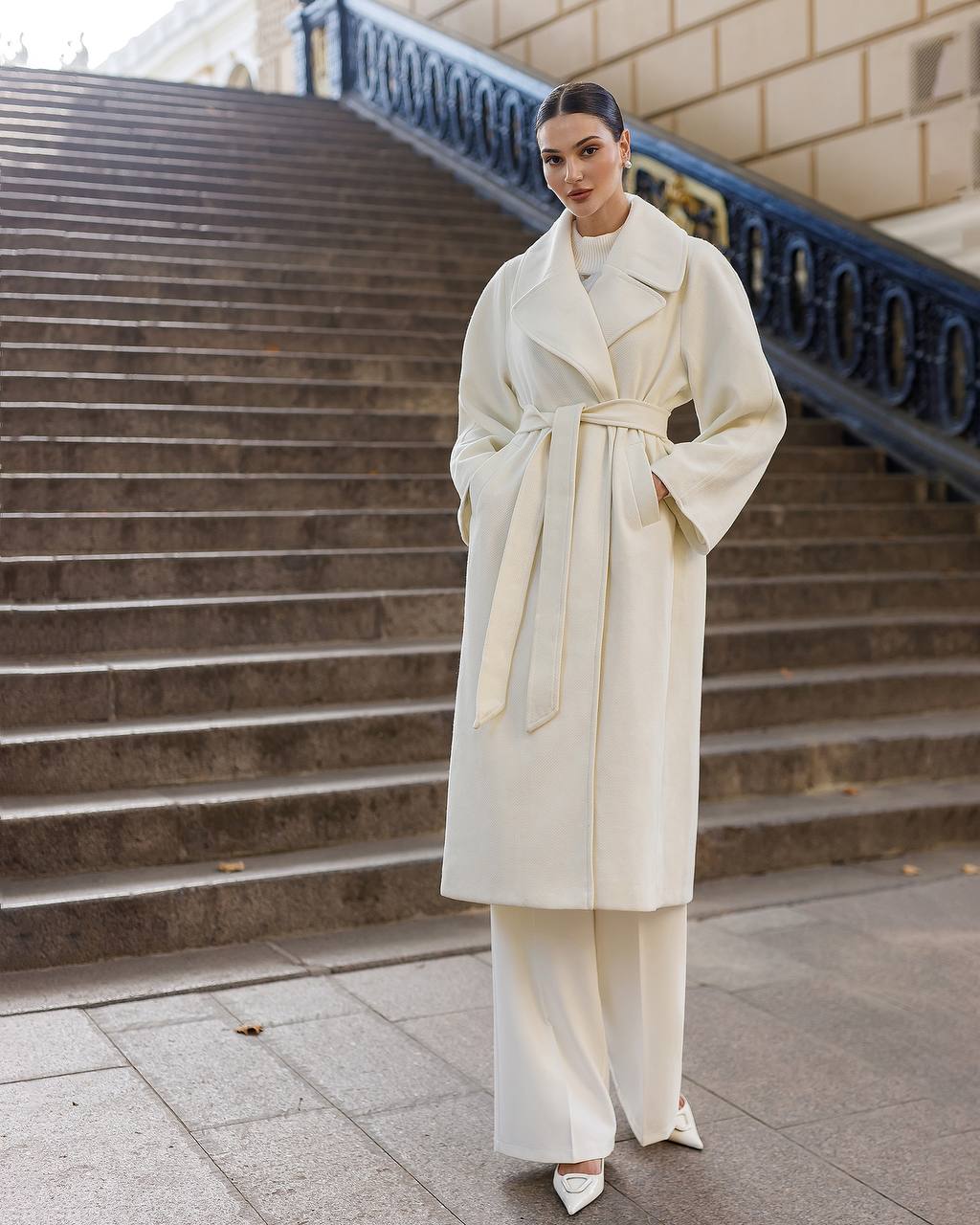Woman in a long cream coat standing on steps outdoors
