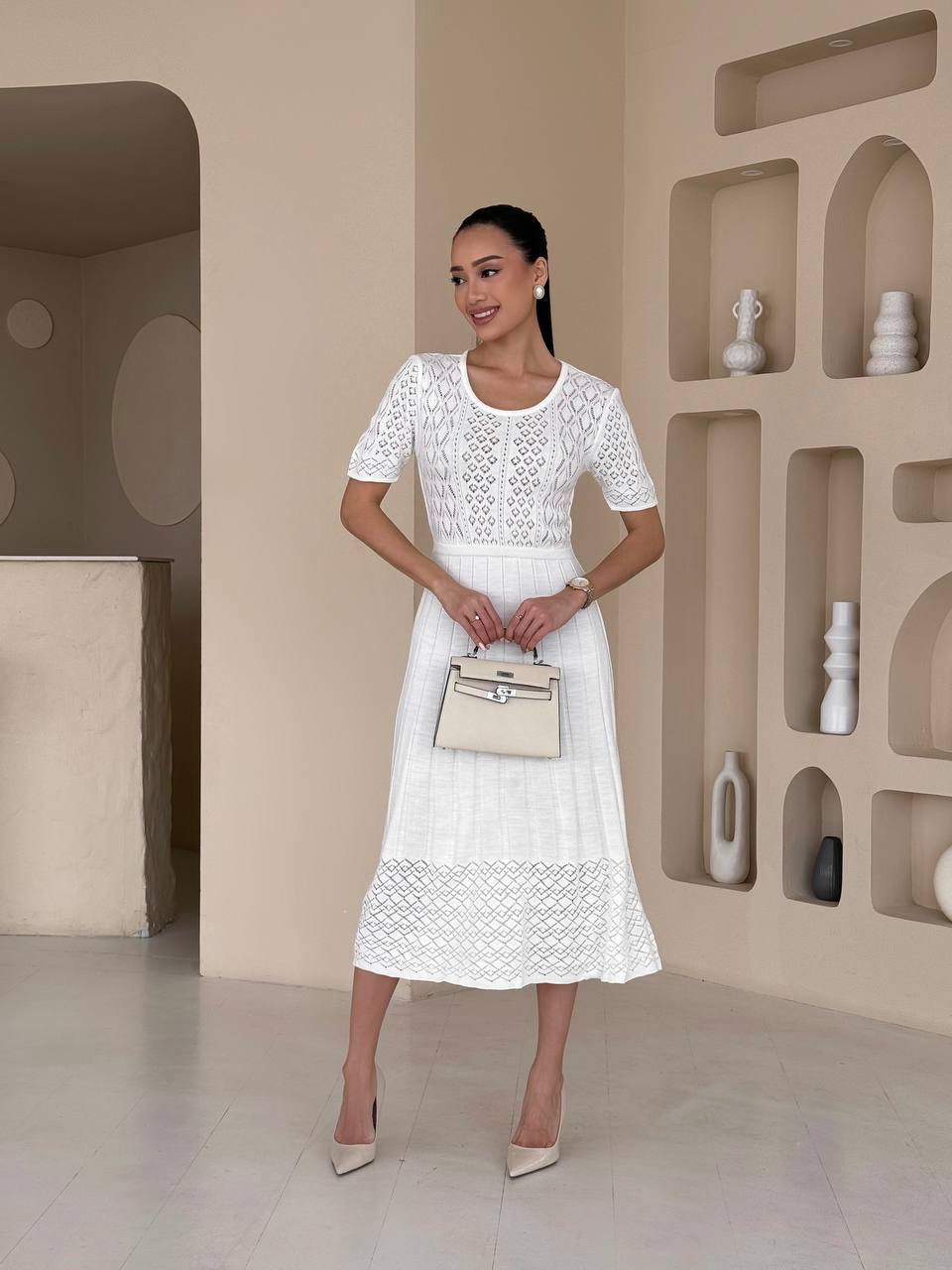 Woman in a white lace dress standing in a modern interior setting.