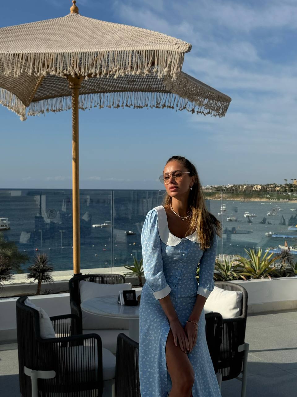 Woman in a blue dress standing under a large umbrella with a scenic background