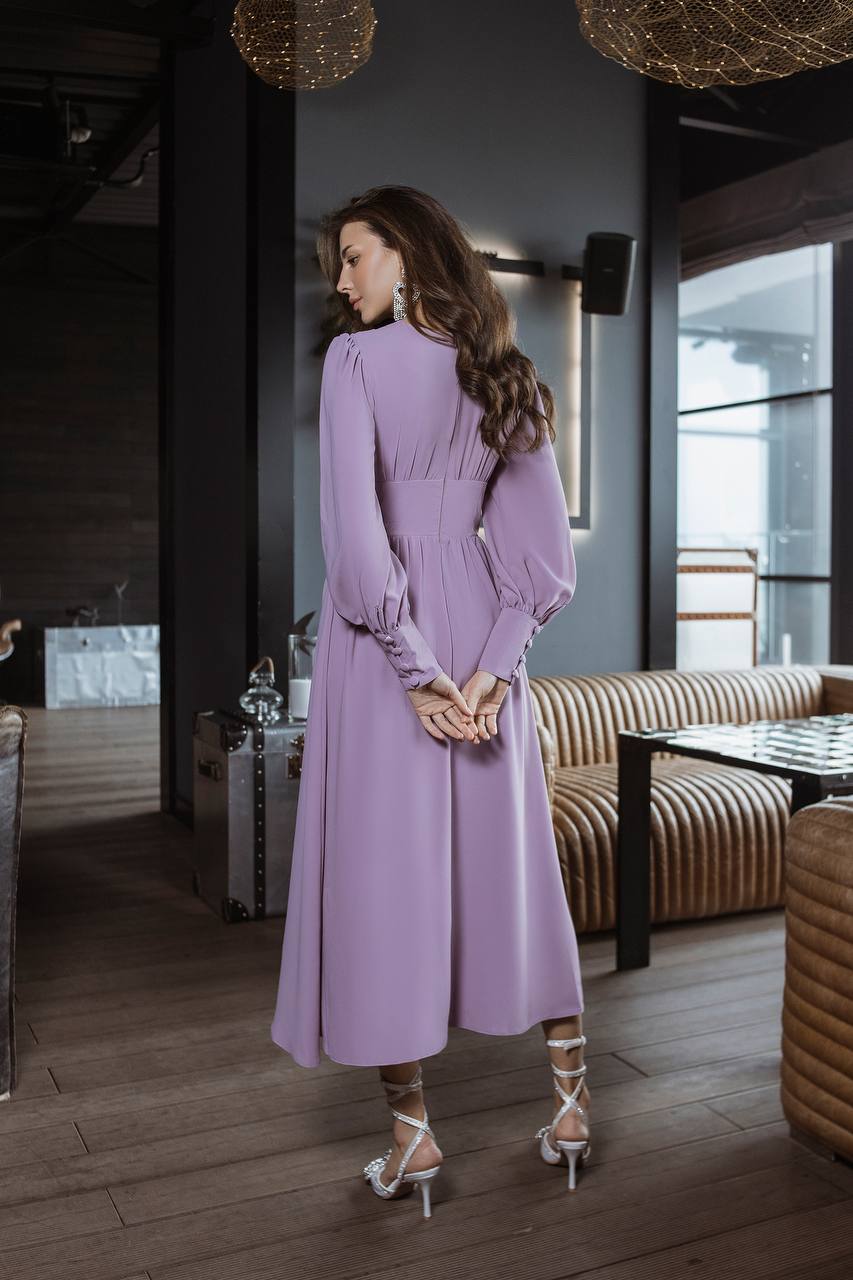 Woman in a purple dress standing in an indoor setting with modern decor.