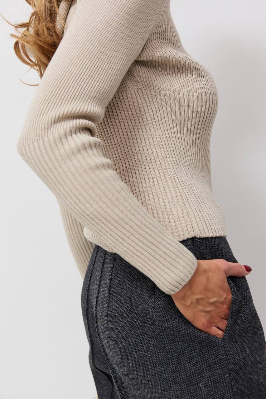 Person wearing a beige ribbed sweater and gray pants on a white background