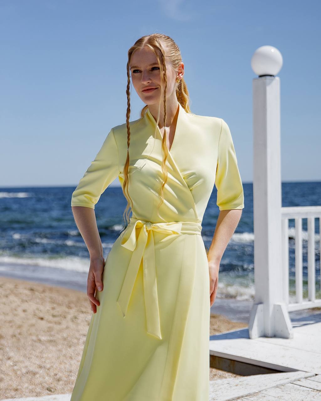 Woman in a yellow dress standing on a beach with ocean and clear sky in the background