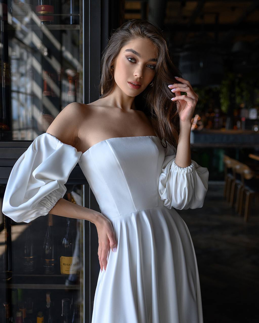 Woman in a white dress standing in a dimly lit bar.