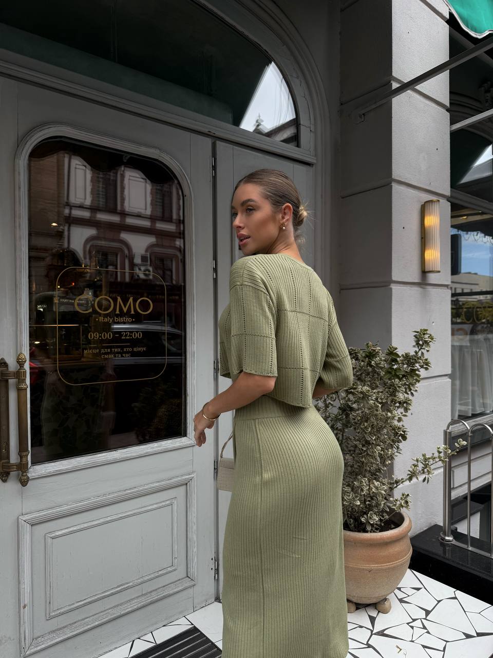 Woman in a green dress standing outside a building with 'COMO' branding.