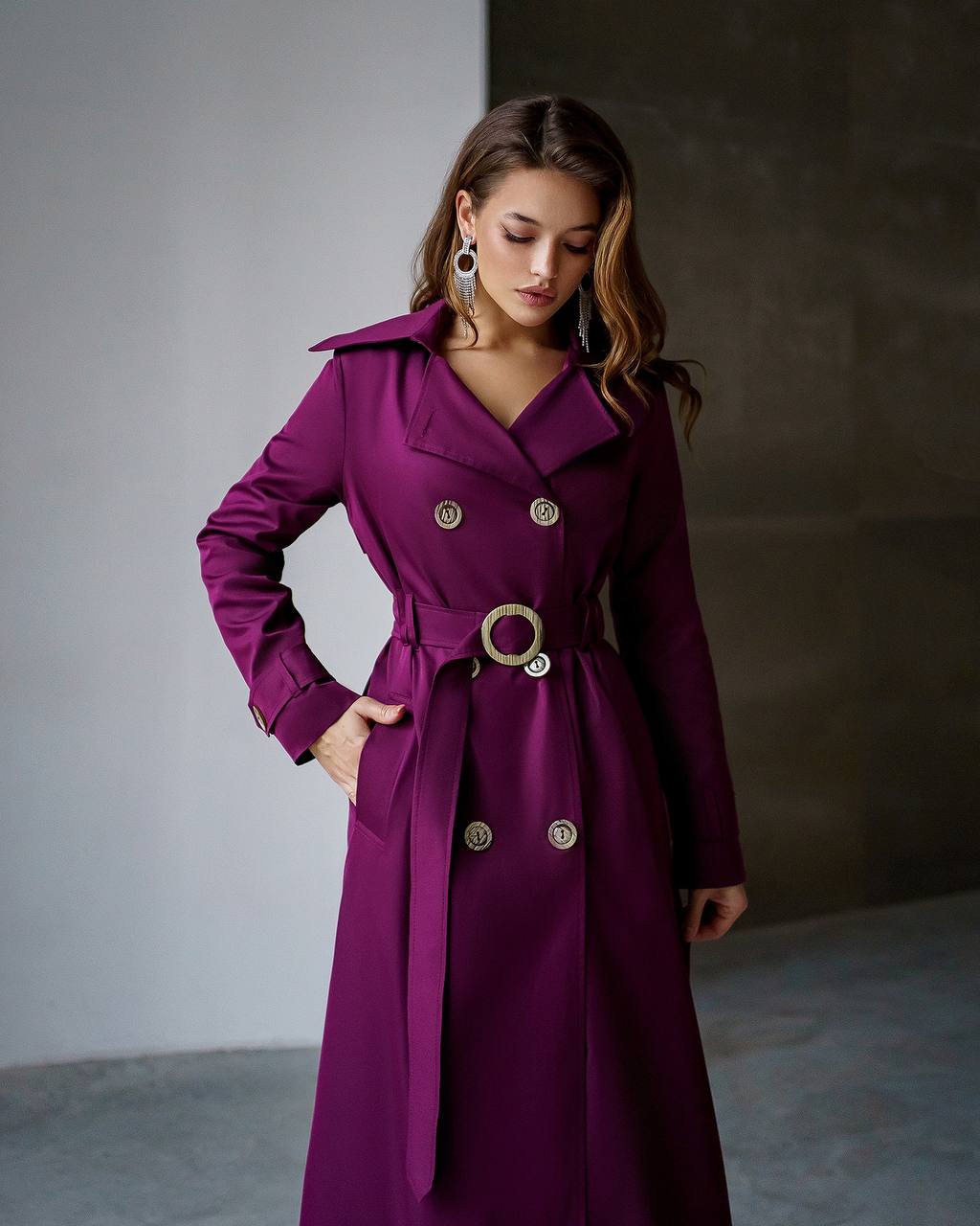 Woman wearing a purple trench coat with gold buttons against a neutral background
