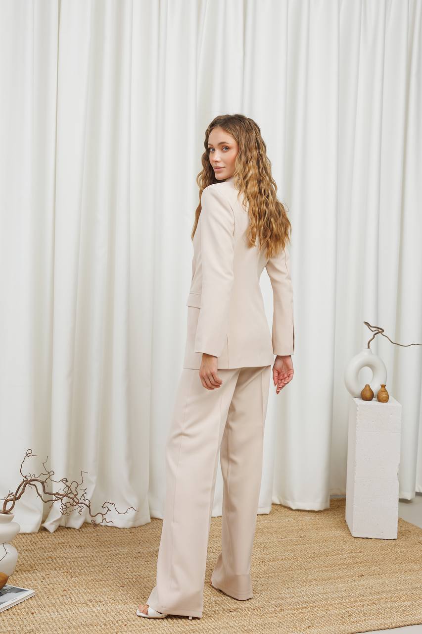 Woman in a beige suit standing in front of white curtains