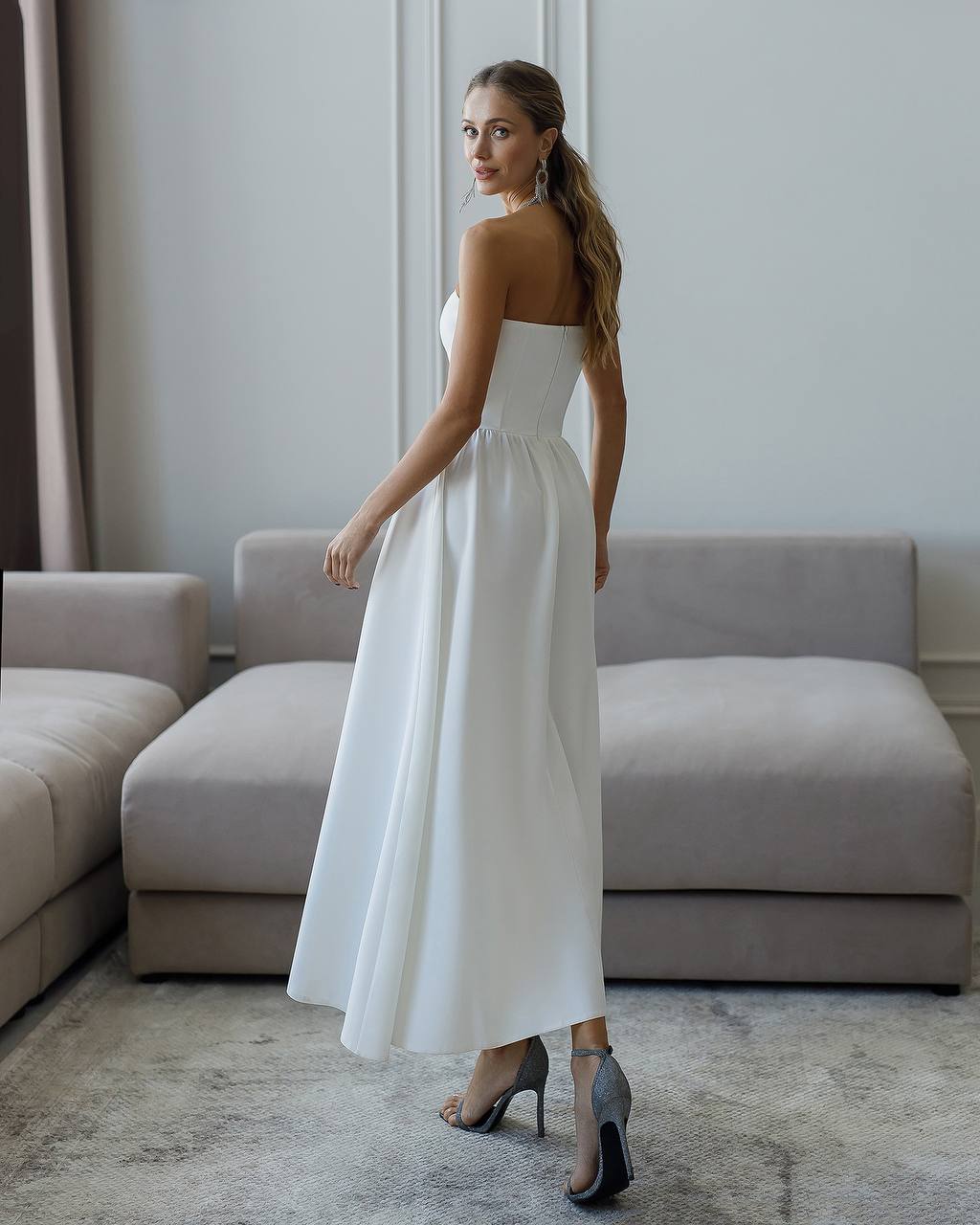 Woman in a white strapless dress standing in a modern living room.