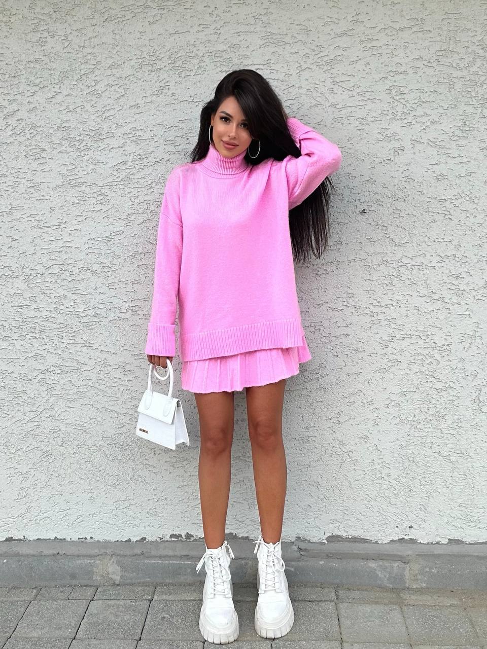 Woman in a pink outfit standing against a gray wall