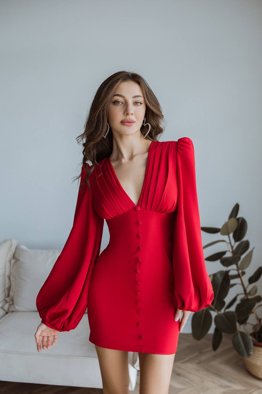 Woman wearing a red dress with puffed sleeves in an indoor setting.