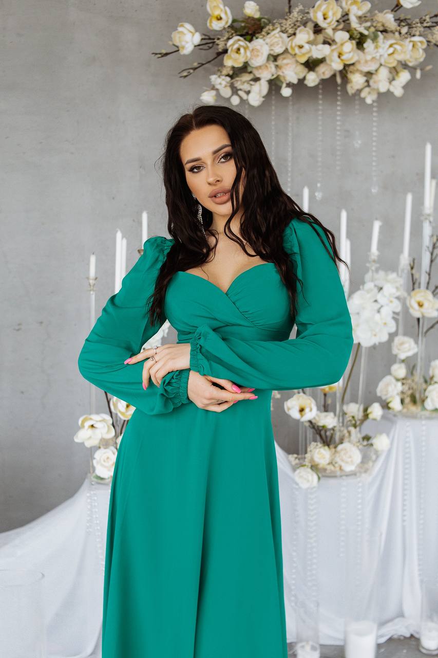 Woman in a green dress standing in a decorated room with flowers and candles.