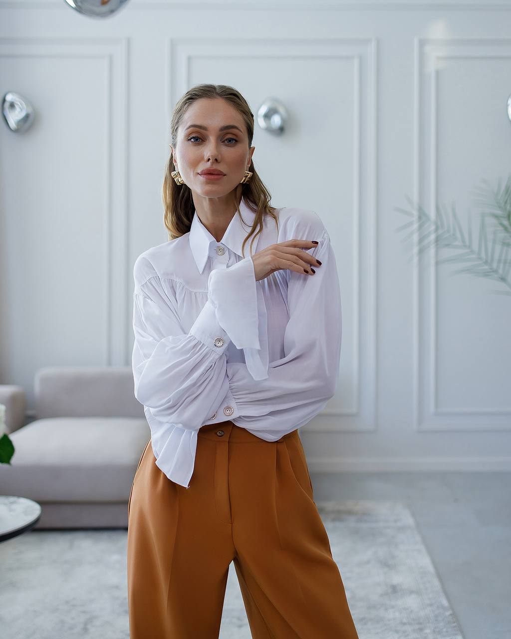 Woman wearing a white blouse and mustard pants in a modern living room.