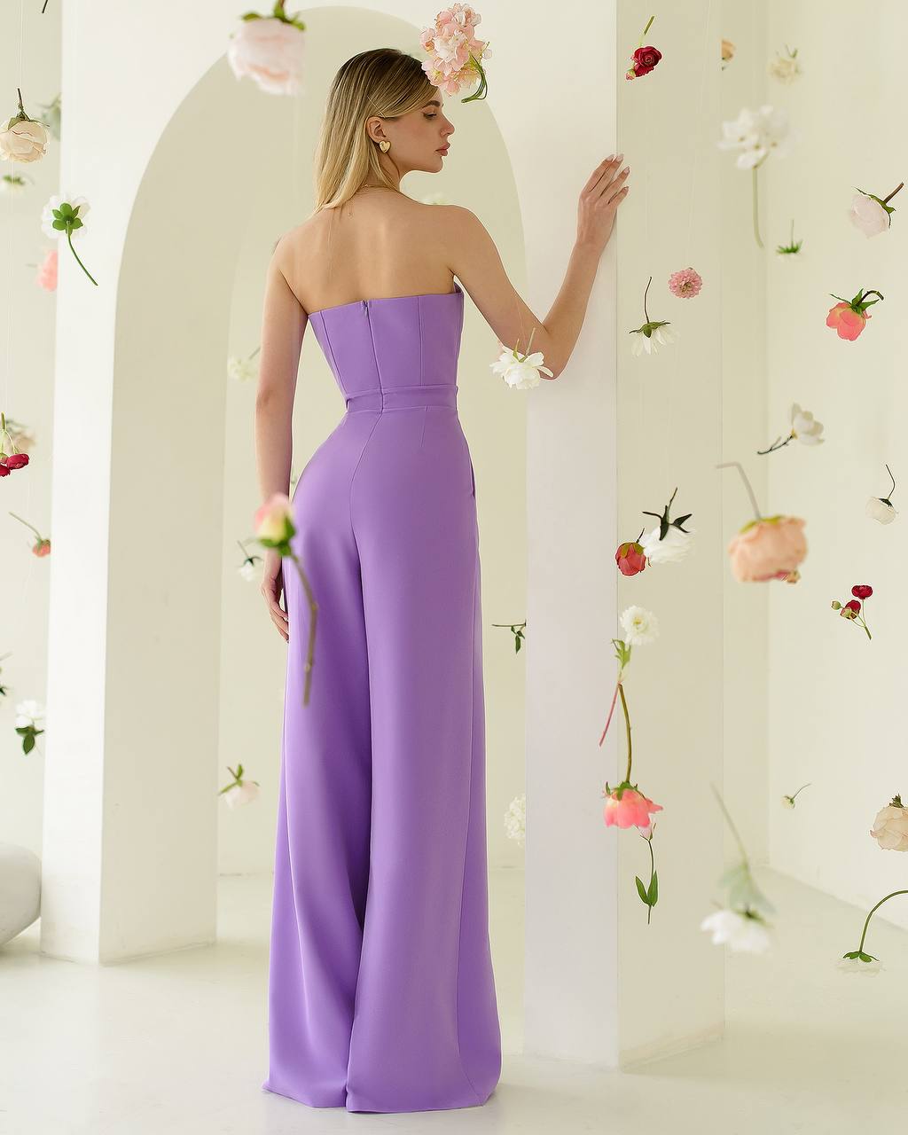 Woman in a strapless purple gown standing against a floral decorated wall.