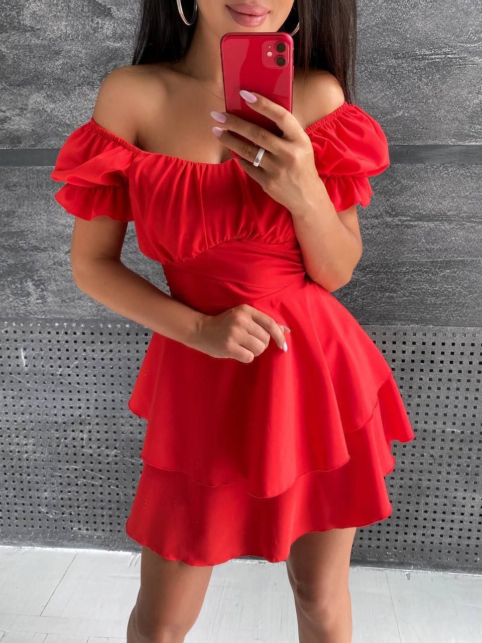 Woman wearing a red off-shoulder dress against a gray wall.