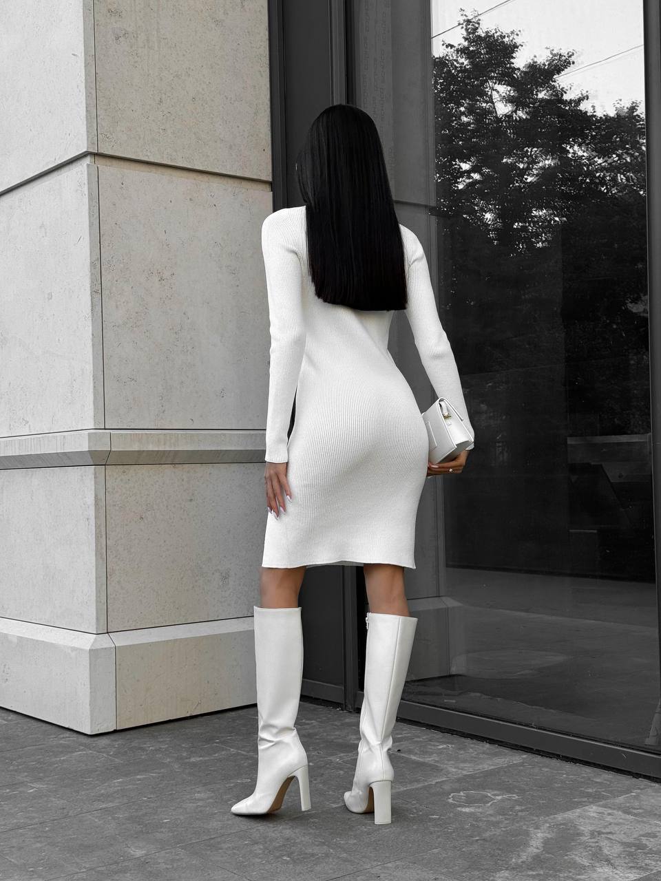 Woman in a white dress and knee-high boots standing in front of a building.