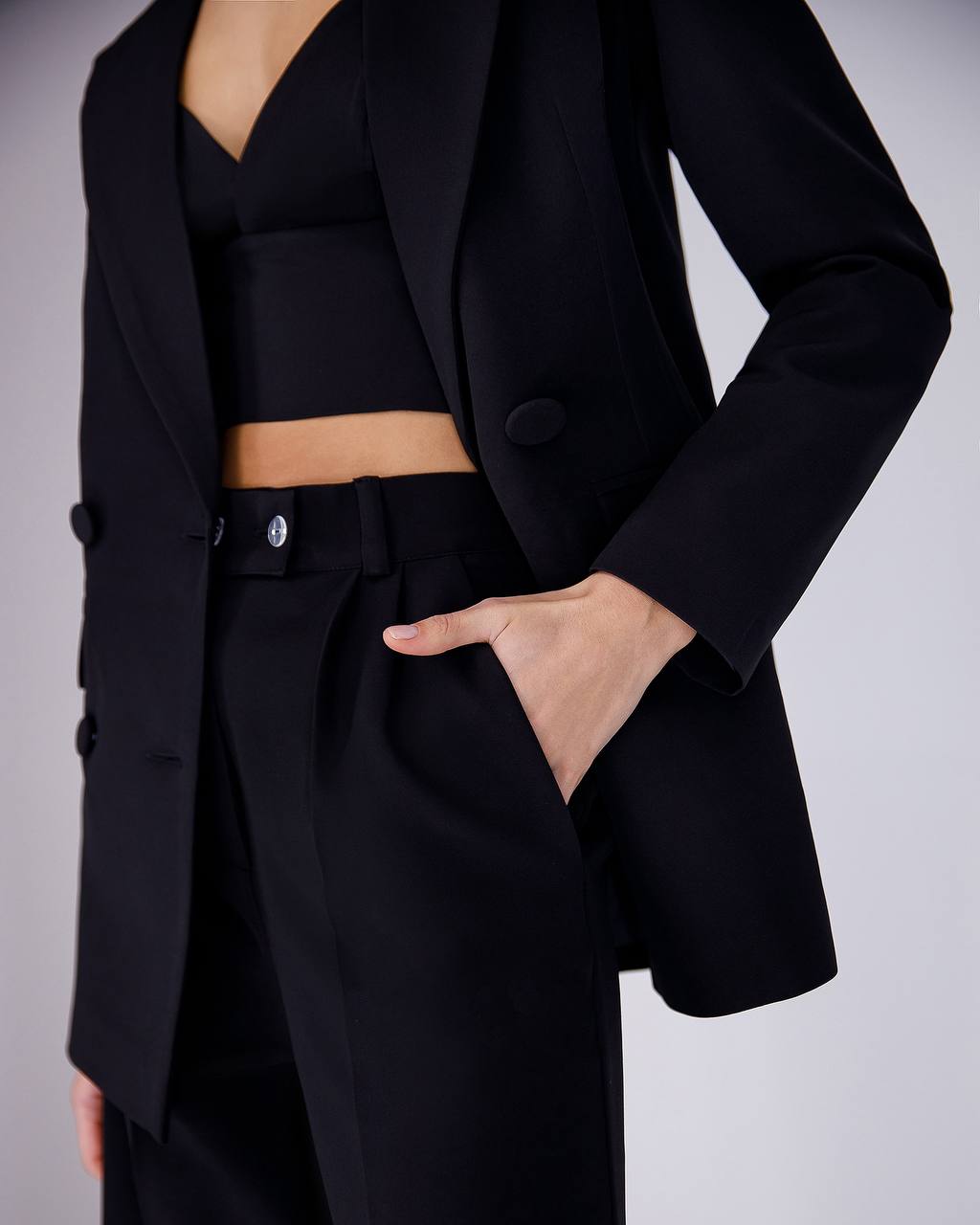 Person wearing a black suit with a cropped top against a gray background