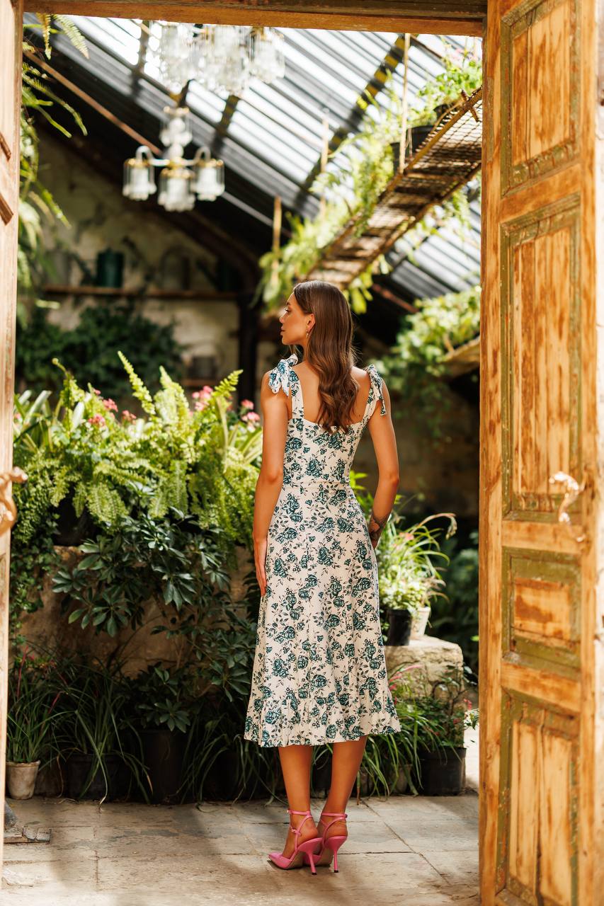 Woman in a floral dress standing in a garden with a wooden door open