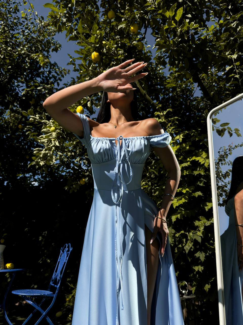 Woman in a light blue dress standing outdoors with trees and a chair in the background