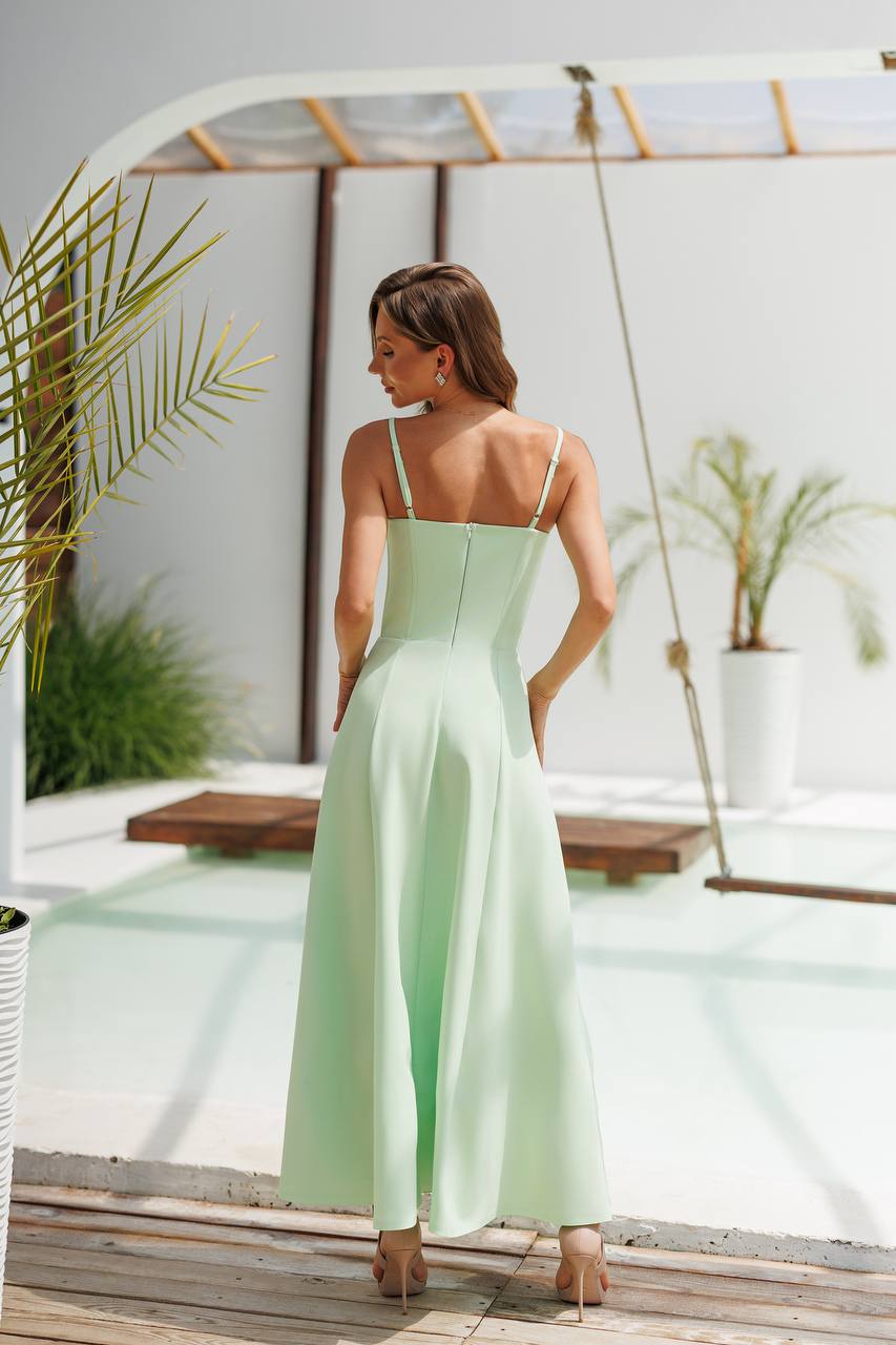 Woman in a light green dress standing by a pool with plants in the background