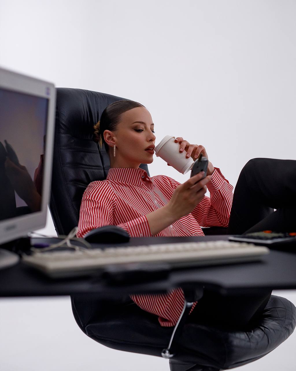 Woman sitting at a desk with a laptop, phone, and coffee cup.