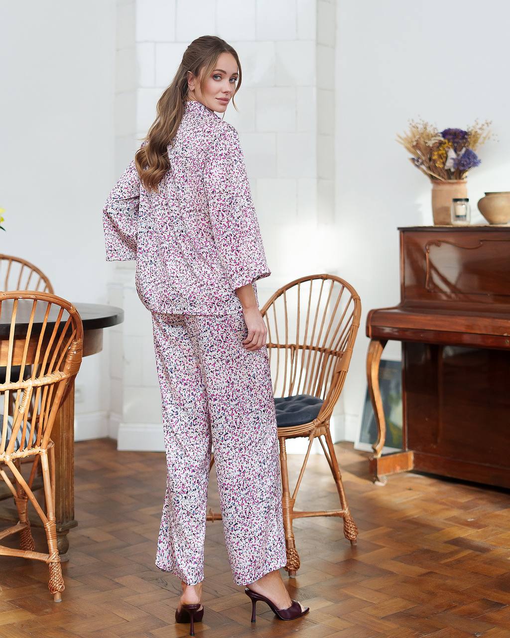 Woman in a floral pajama set standing in a room with wooden furniture and a piano.