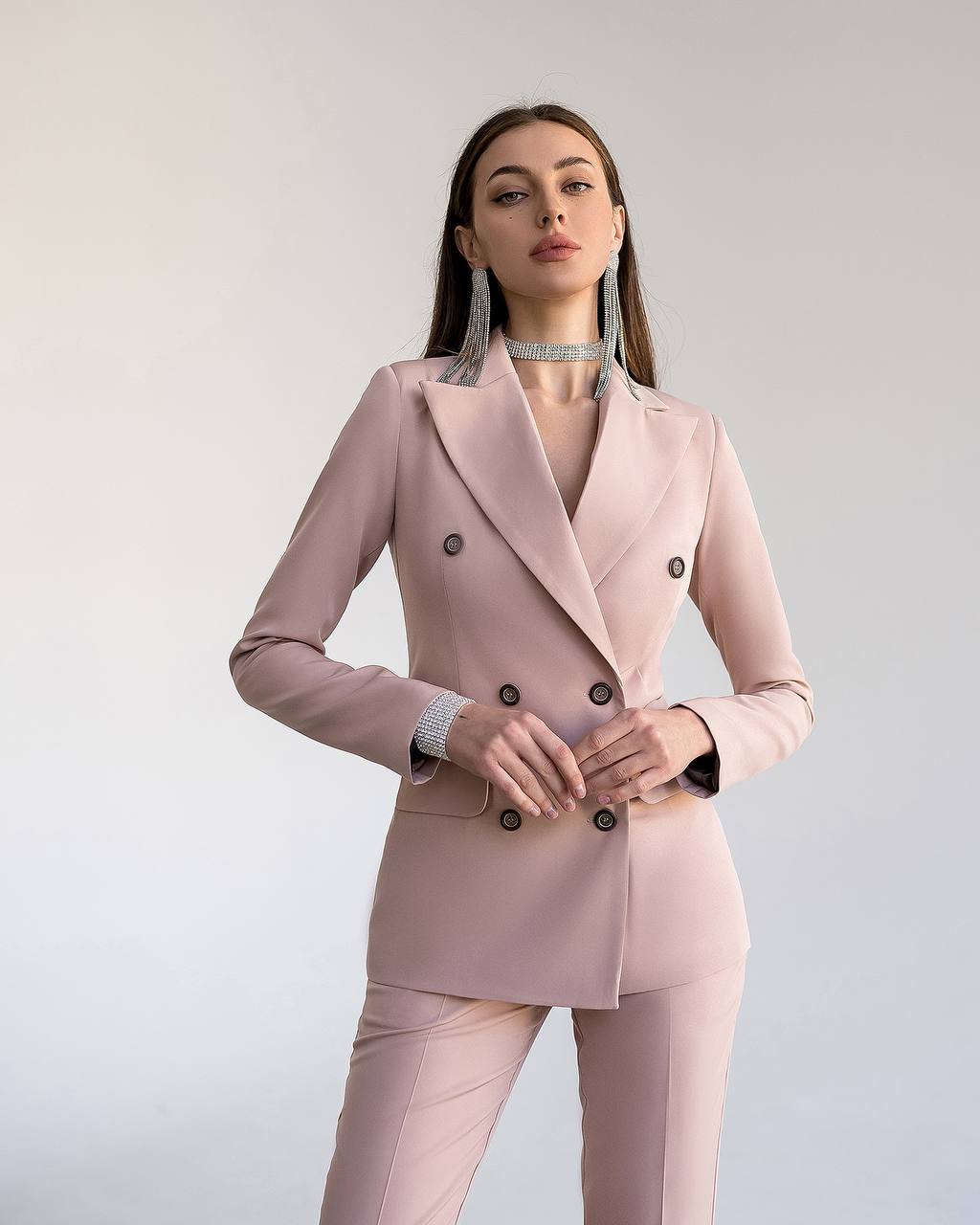 Woman wearing a pink suit with black buttons against a light gray background