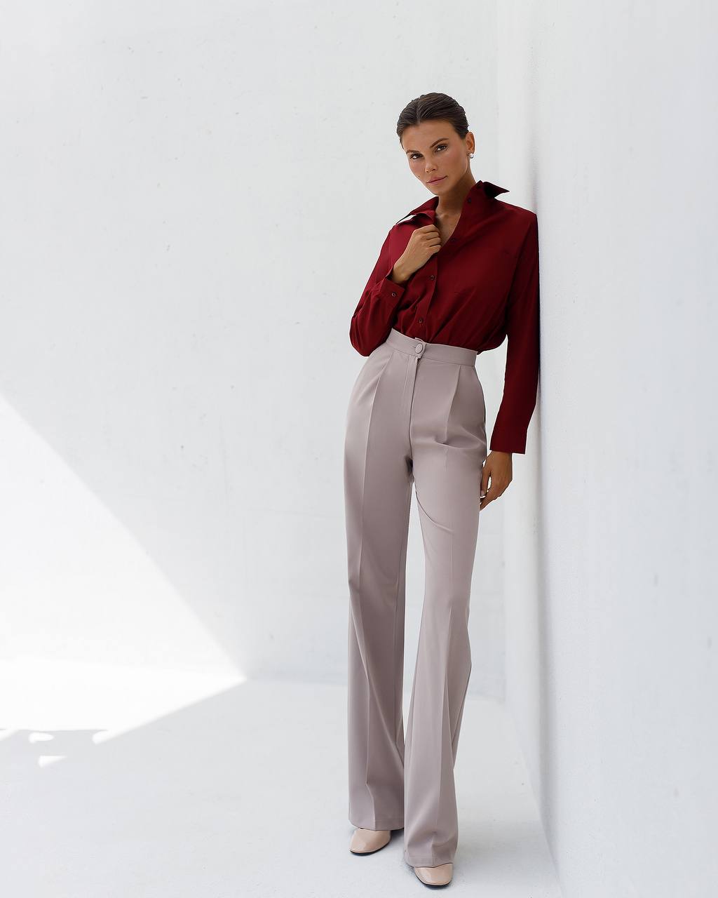 Woman wearing a burgundy blouse and light gray pants against a white background