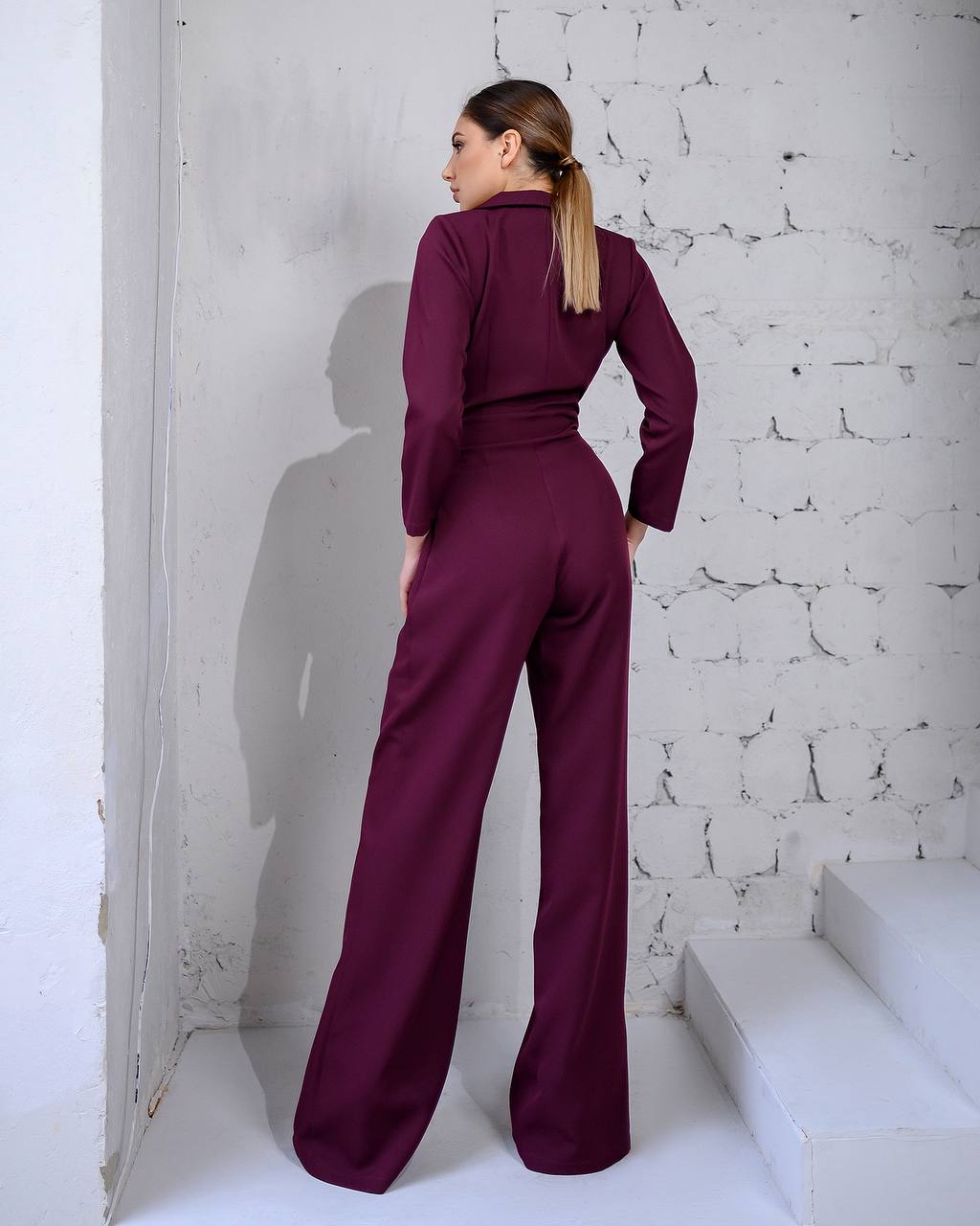 Woman wearing a maroon outfit standing against a textured white wall.